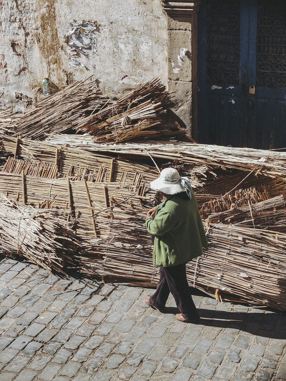 person walking past brown wood pile on side of road