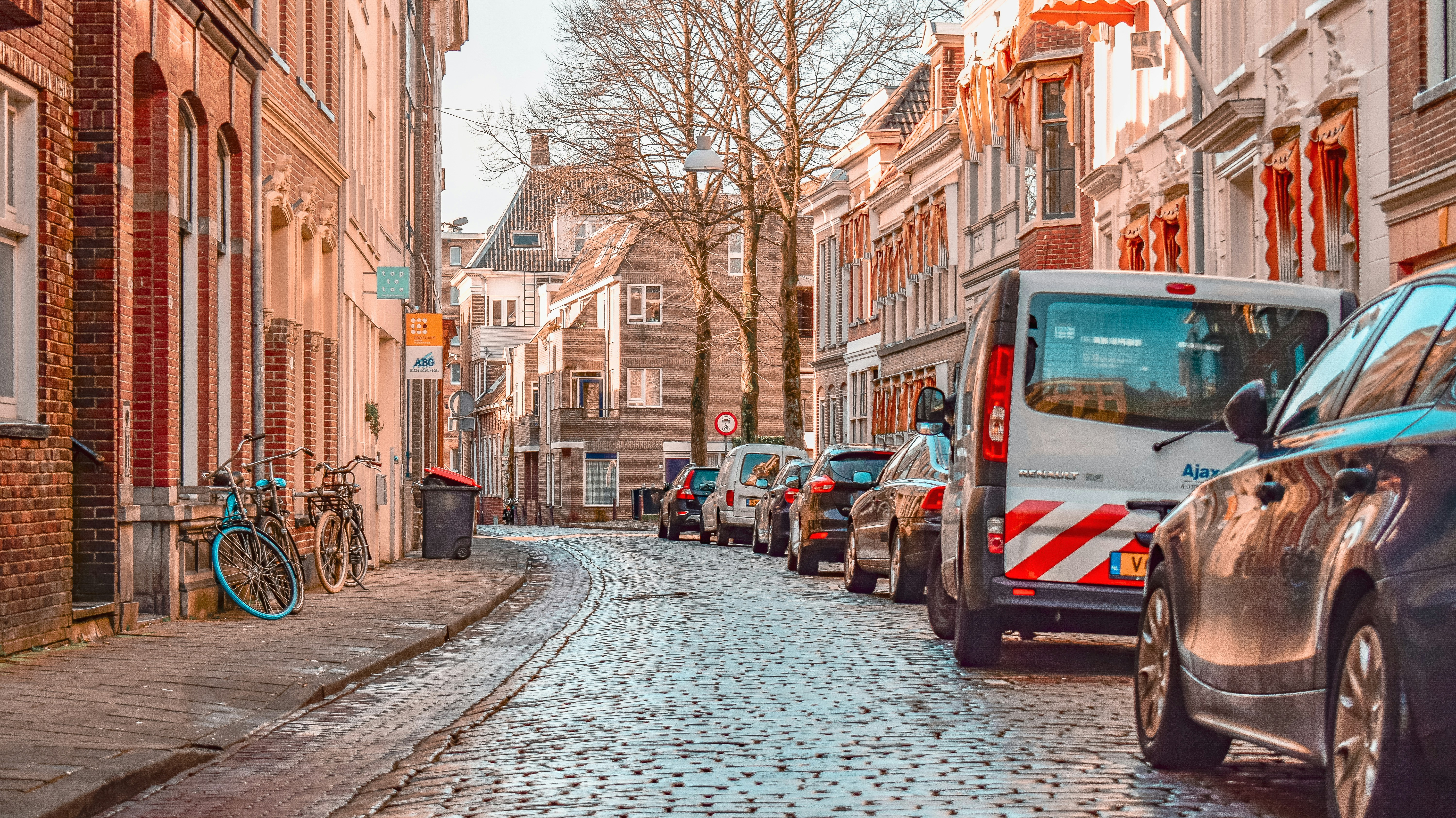 Auto's en fietsen geparkeerd langs een smalle Europese straat met kinderkopjes.