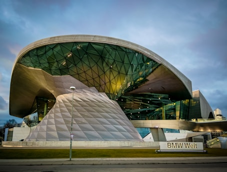 A futuristic building with a large, curved glass and metal structure, featuring geometric patterns and reflective surfaces. The architecture is innovative and modern, with clean lines and an expansive shape.