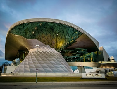 A futuristic building with a large, curved glass and metal structure, featuring geometric patterns and reflective surfaces. The architecture is innovative and modern, with clean lines and an expansive shape.
