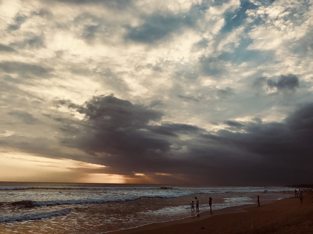 people standing on seashore during golden hour