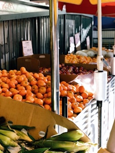Colorful seasonal fruits and vegetables stacked together in a bright outdoor market stall.