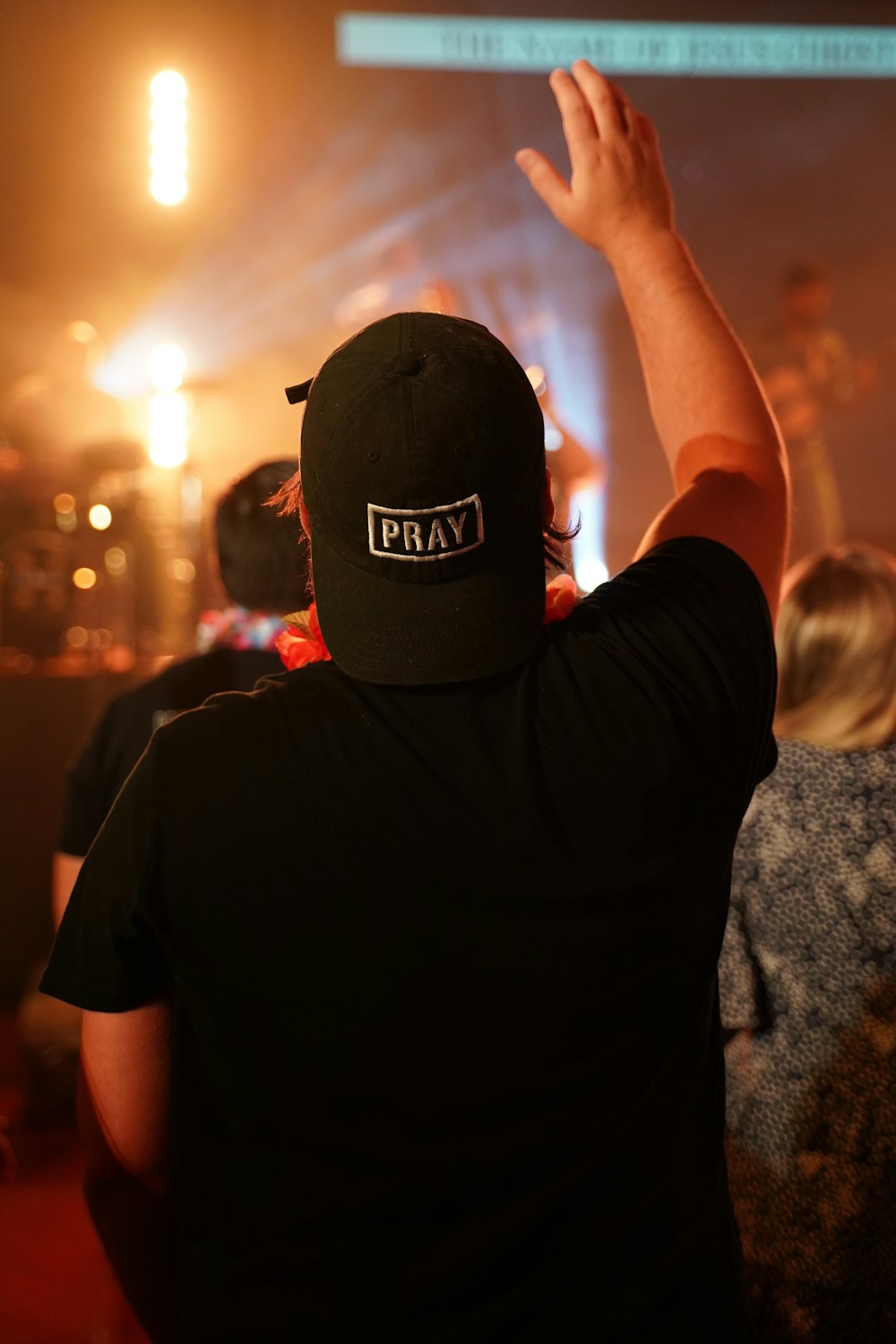 standing man wearing black Pray cap raising right hand