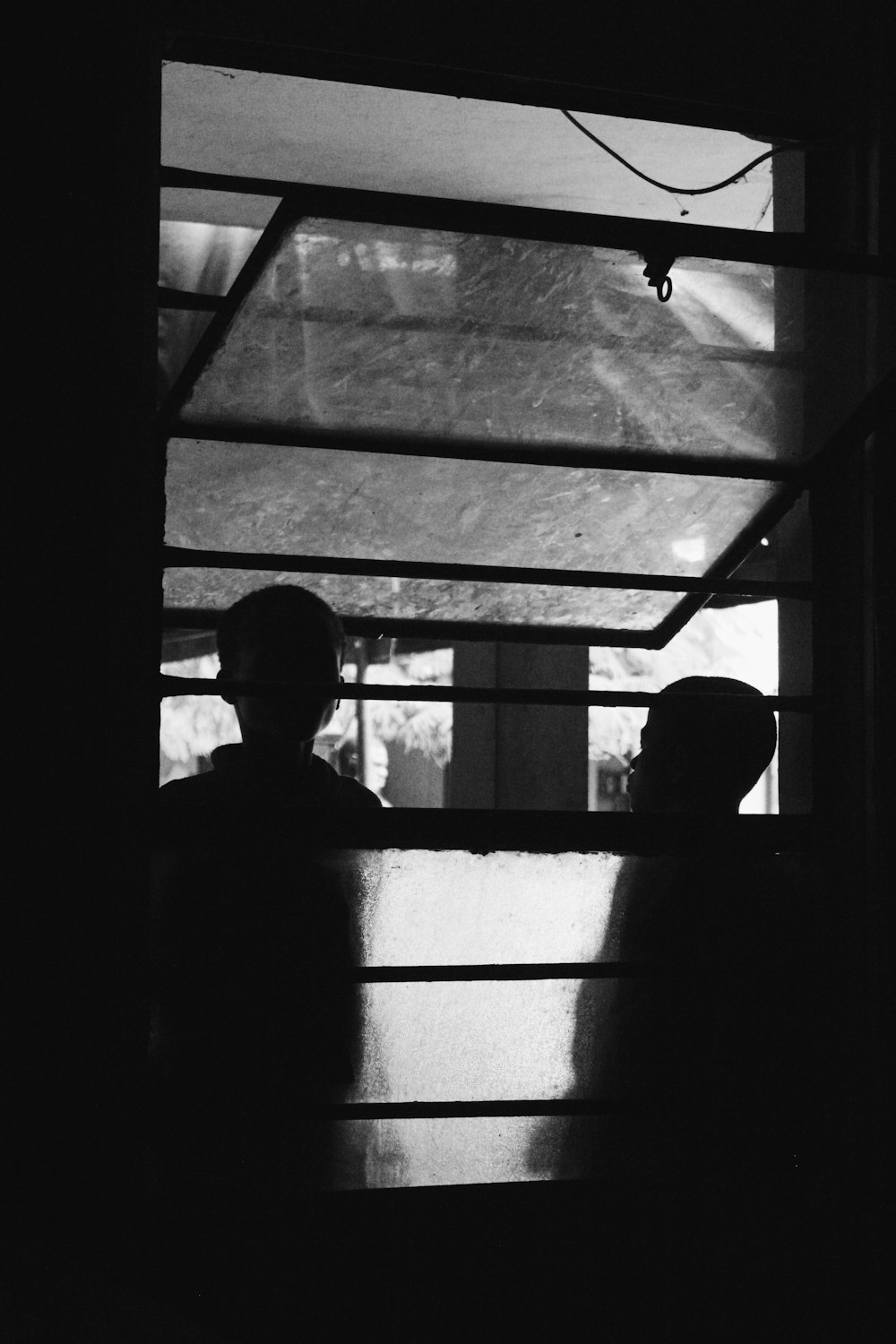 grayscale photography of two persons standing outside window