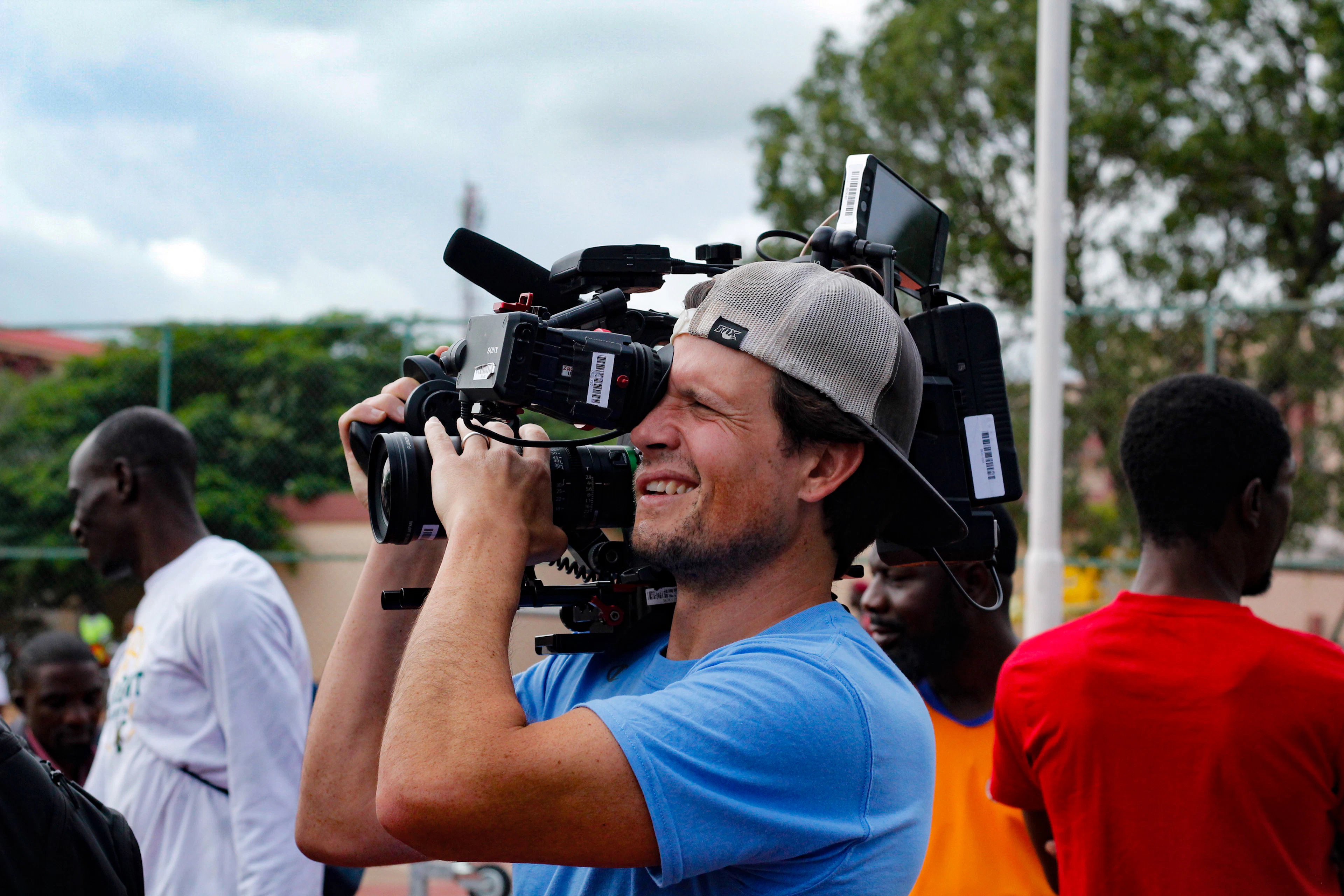 A camera operator grinning while filming at an outdoor event