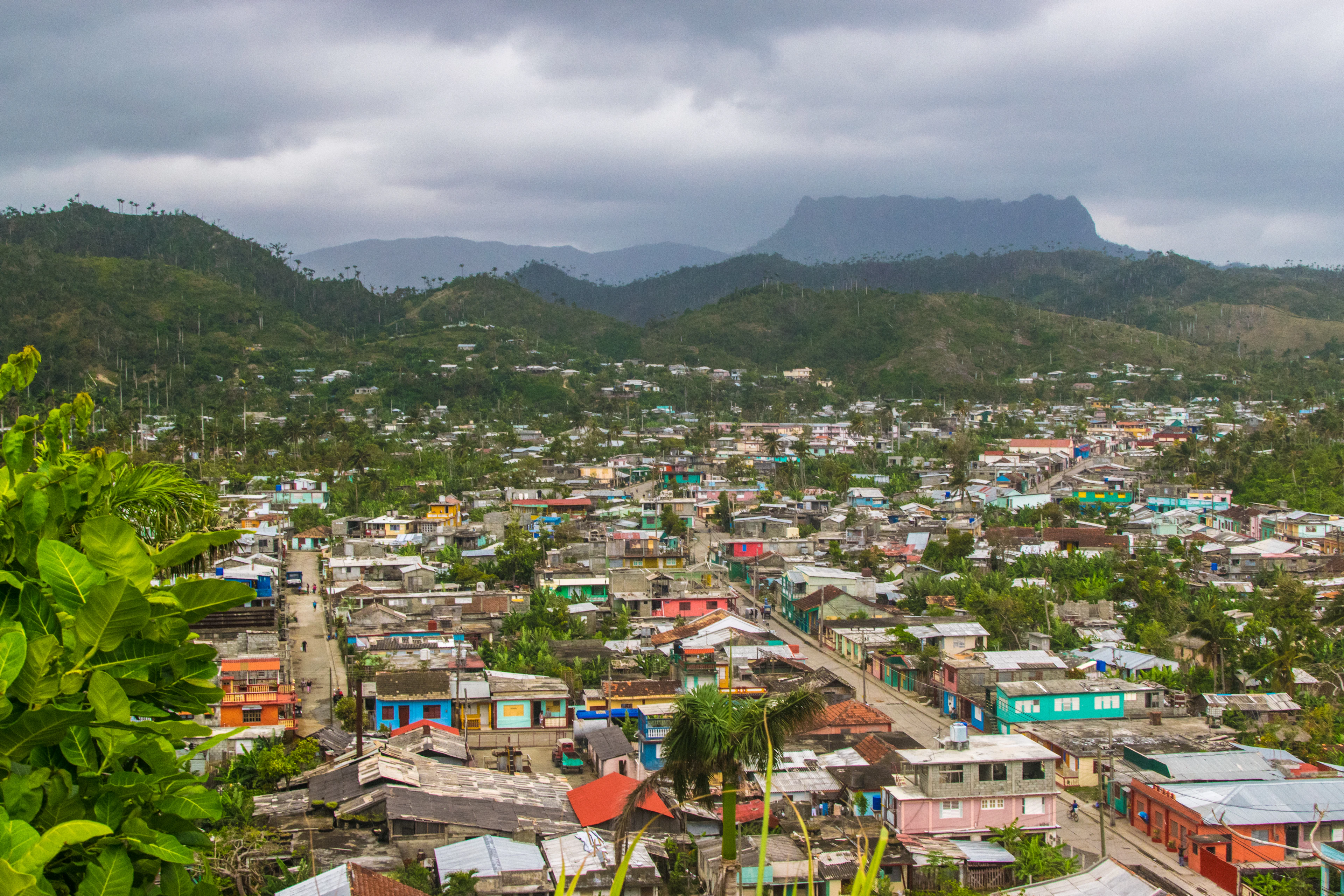 The rooftops of Baracoa among palms, with the flat-topped mountain of El Yunque beneath the clouds beyond