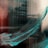 A dynamic brushstroke of teal paint sweeps diagonally across a reflective surface, with blurred reflections of a building in the background. The combination of colors and abstract form creates a sense of movement and fluidity.