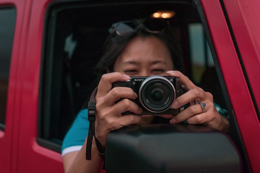 mujer sosteniendo una cámara DSLR en un vehículo rojo