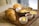 A breakfast presentation featuring a croissant, small frying pan with fried eggs and vegetables, small bowls containing butter, jam, and what appears to be cheese, all arranged on a wooden cutting board.