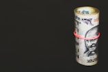 A rolled-up bundle of Indian currency notes secured with a red rubber band is placed against a solid, dark background. The banknotes prominently feature a portrait of Mahatma Gandhi.