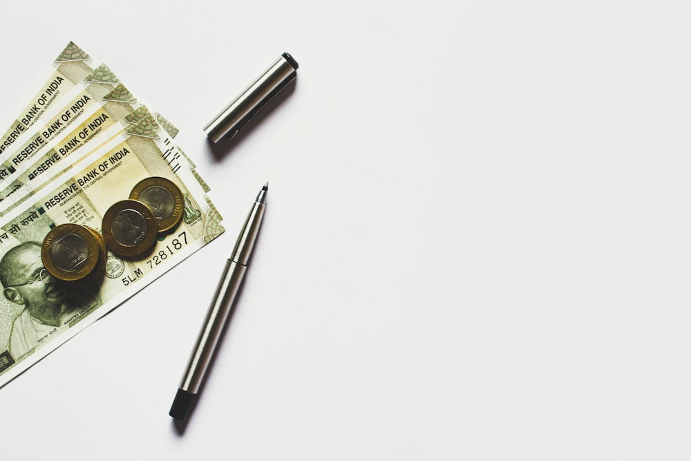 stylo gris à côté des pièces de monnaie sur les billets de banque en roupies indiennes