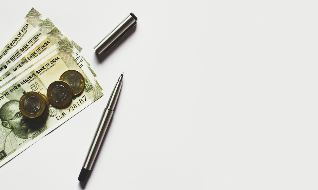 gray pen beside coins on Indian rupee banknotes