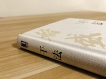 A hardcover book with Asian characters on its spine and cover is placed on a wooden surface. The book is predominantly white with a textured appearance, and features subtle gold patterns.