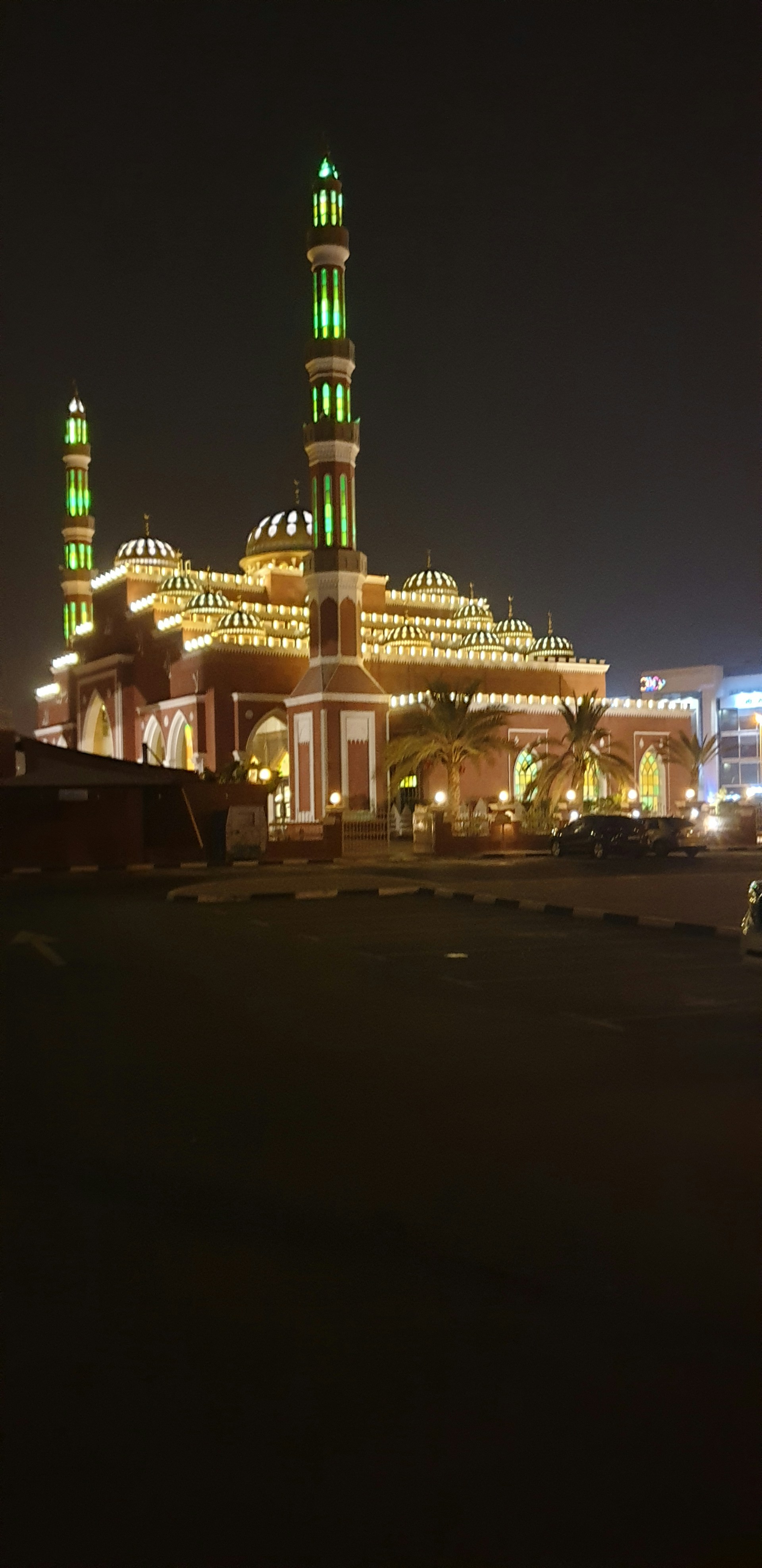 The majestic Masjid Nabawi illuminated at night, showcasing its iconic green dome and bustling courtyard.