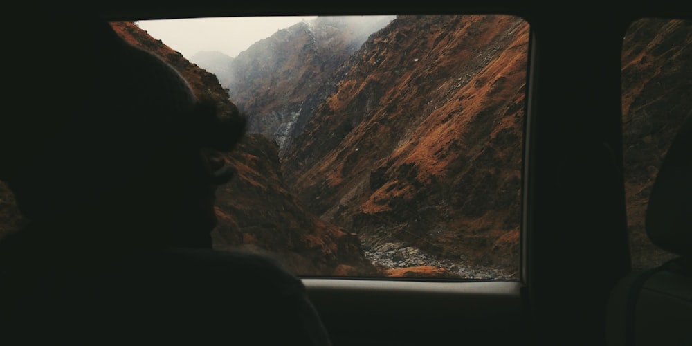 a person looking out a window at mountains