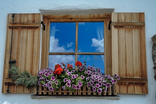 A rustic wooden planter filled with vibrant flowers on a sunny windowsill.