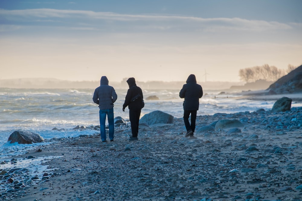 three people in black coats walking on shore