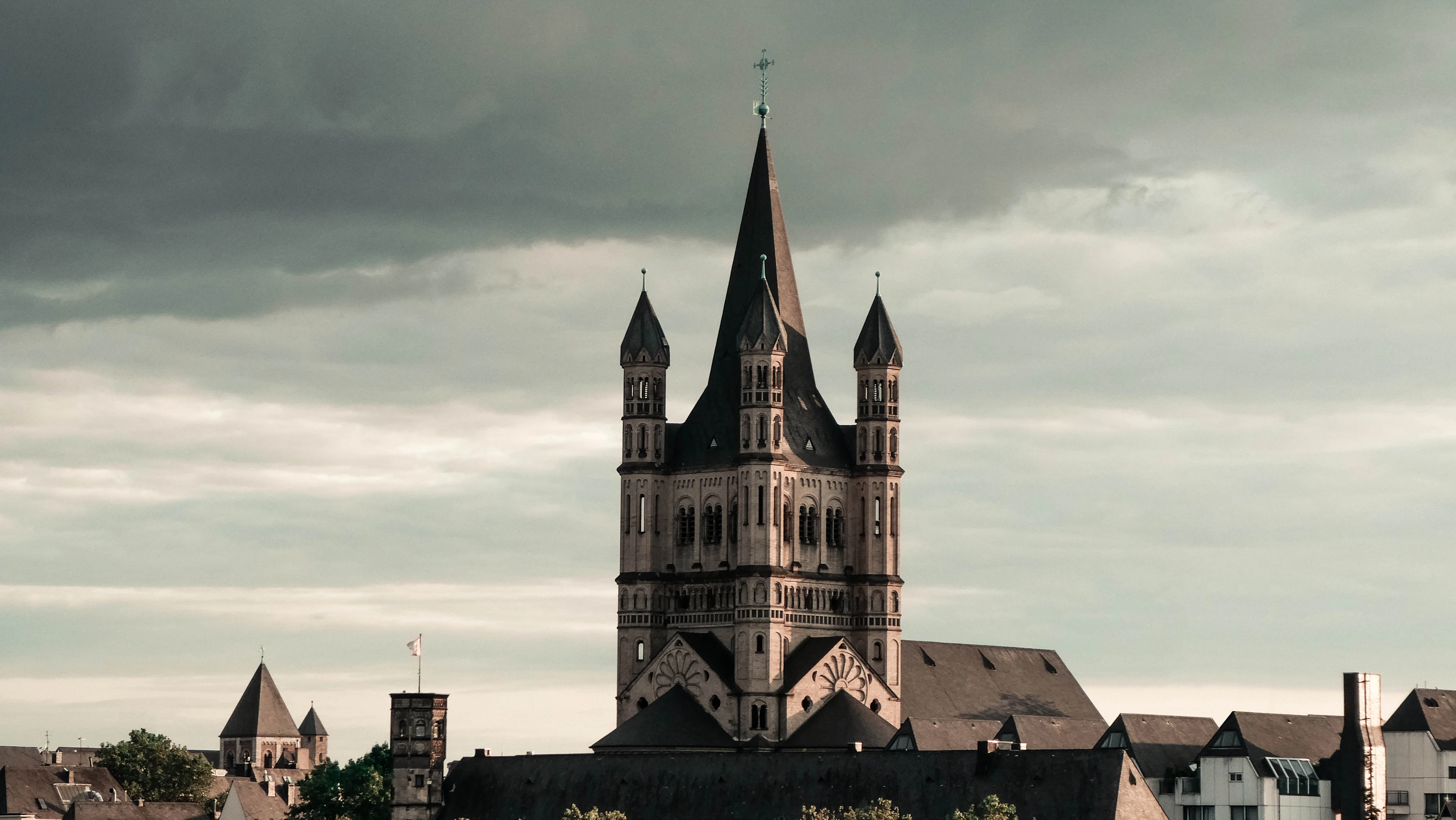 Great St. Martin church's tower rising over Cologne's rooftops under a dramatic, stormy sky.
