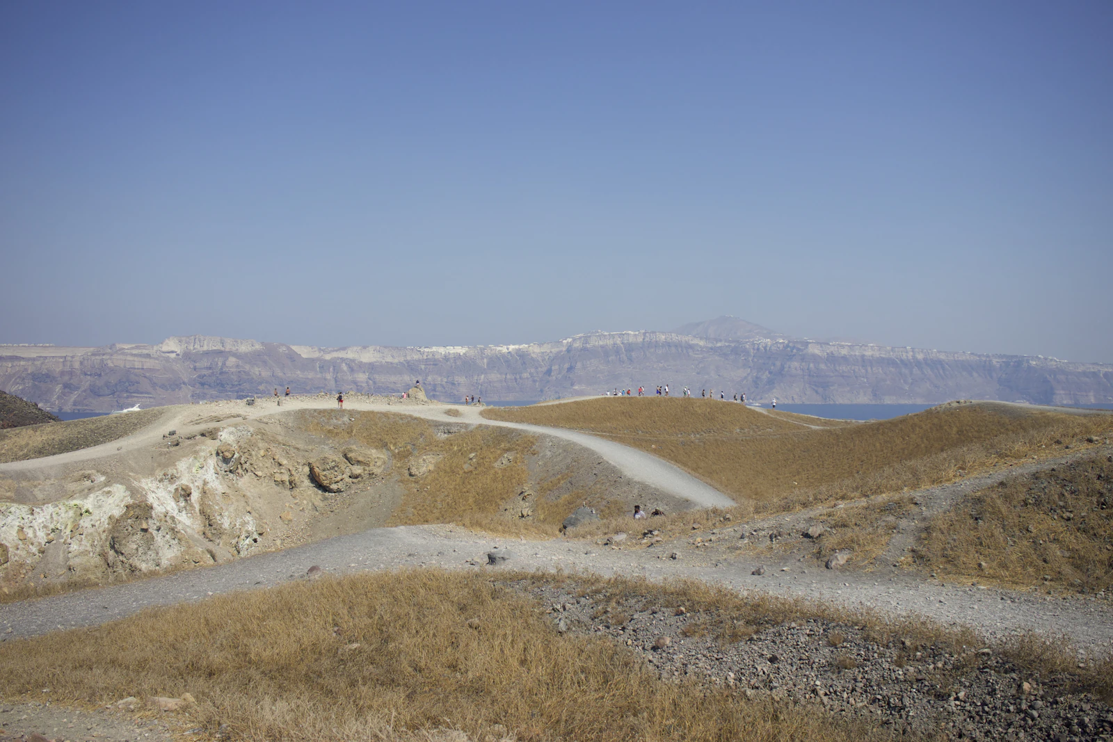 A dirt track running along a dry ridge with the caldera cliffs and the sea behind it.