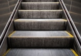An escalator with metal steps, lined with yellow edges, ascending between two metallic walls.