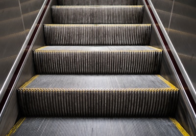 An escalator with metal steps, lined with yellow edges, ascending between two metallic walls.
