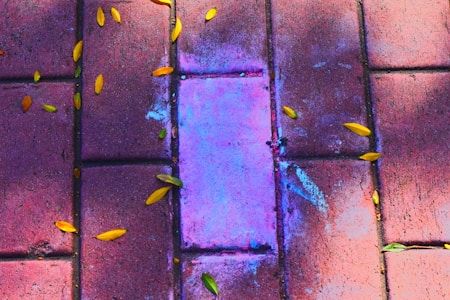 A concrete pavement with a central area stained with vibrant purple and blue hues. Scattered around are small yellow leaves adding an autumnal touch.