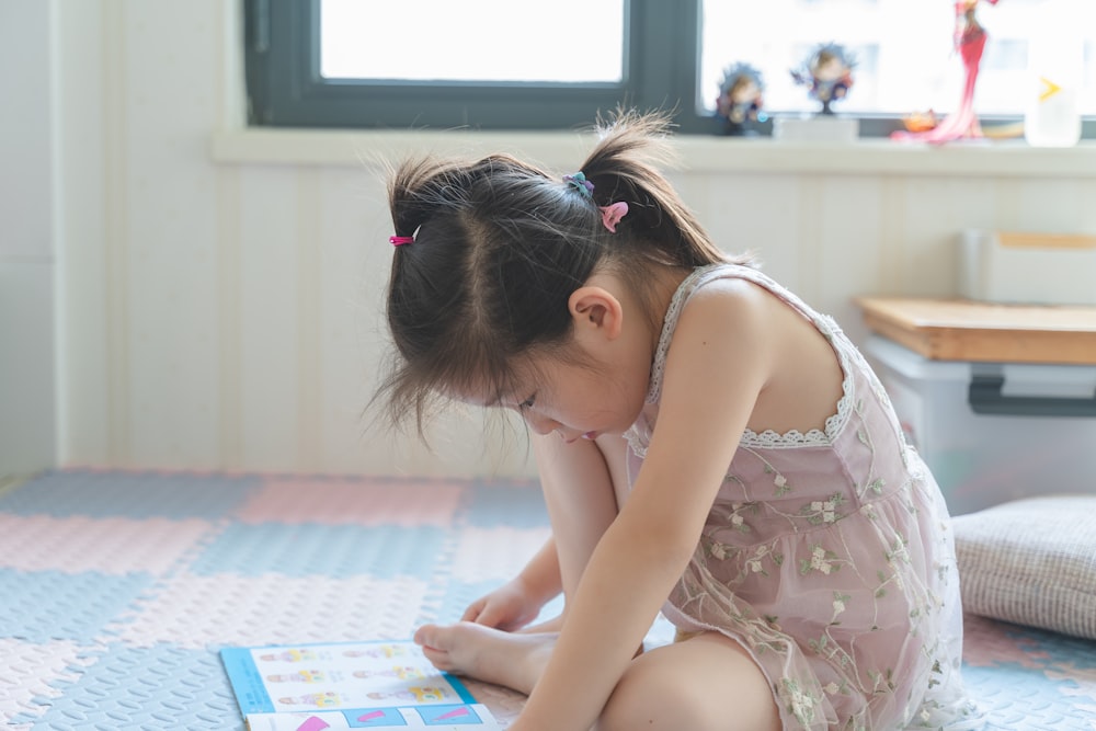 a little girl sitting on the floor reading a book