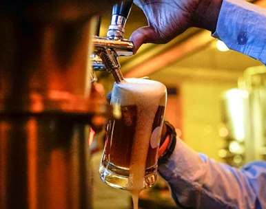 A bartender pouring a craft beer with a frothy head, set against a backdrop of green and gold accents.