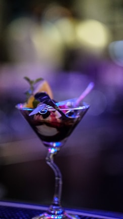 An elegant cocktail glass filled with a colorful layered drink, set against a softly lit background.