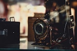 A vintage camera is prominently displayed, its intricate details and metallic components highlighted. The background is softly blurred, giving a nostalgic and classic feel to the setting.