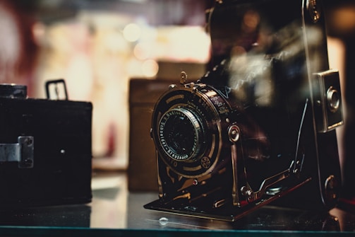 A vintage camera is prominently displayed, its intricate details and metallic components highlighted. The background is softly blurred, giving a nostalgic and classic feel to the setting.