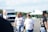 A group of people walking in a parking lot with a U-Haul truck and a white tent in the background. Two individuals are prominently featured in the foreground, one with long blond hair wearing sunglasses and a shirt that reads 'Rose Lavelle is good at soccer,' while the other person has short hair and is wearing reflective sunglasses and a different shirt. Another person to the right has a cap and is wearing a black shirt.