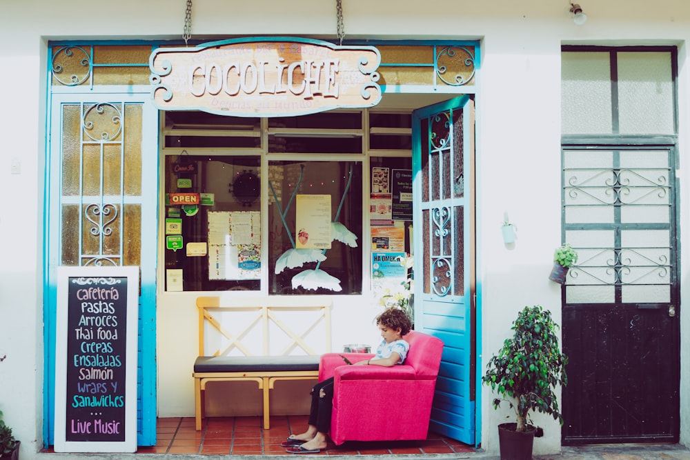 girl sitting on pink sofa chair beside bench