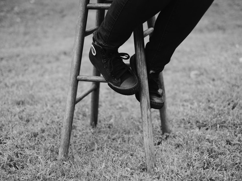 grayscale photo of person sitting on brown stool