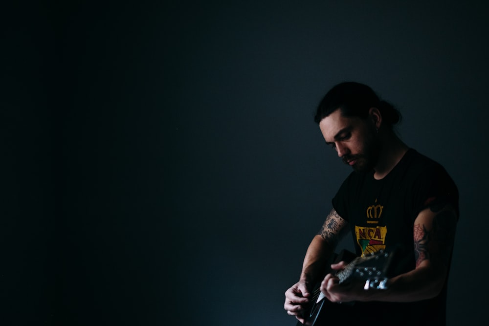 man wearing black crew-neck holding guitar