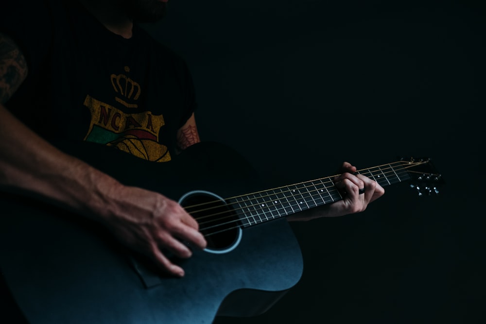 person wearing black and multicolored shirt playing acoustic guitar