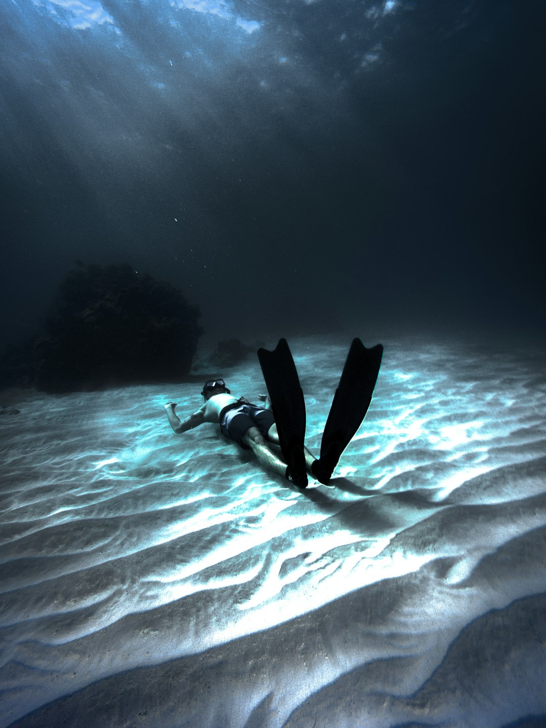 man wearing diving gear lying on sand underwater