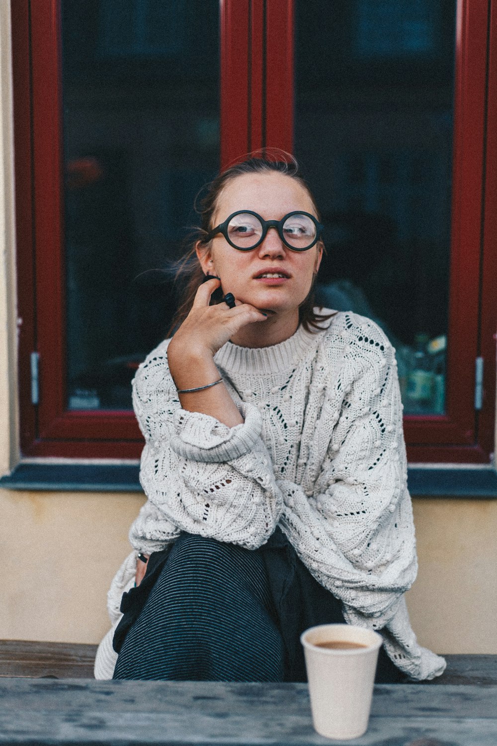 woman in eyeglasses and white sweater sitting in front of coffee cup