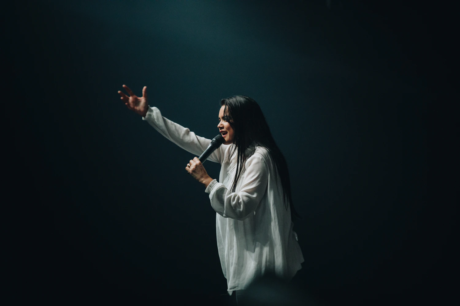 Speaker holding a microphone on a dark stage, addressing an audience