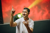 man in white polo shirt pointing index finger on top while smiling