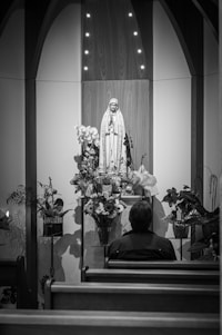 grayscale photography of person sitting in front of religious figure