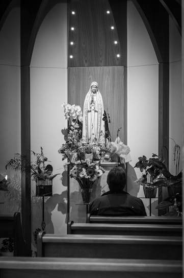 grayscale photography of person sitting in front of religious figure