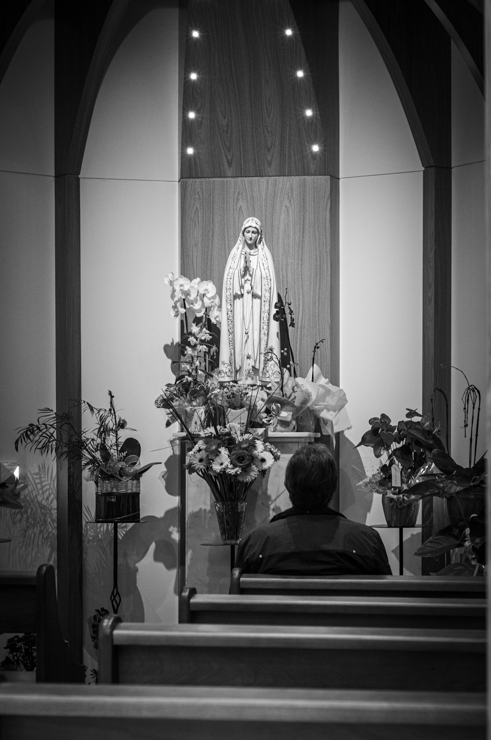 grayscale photography of person sitting in front of religious figure