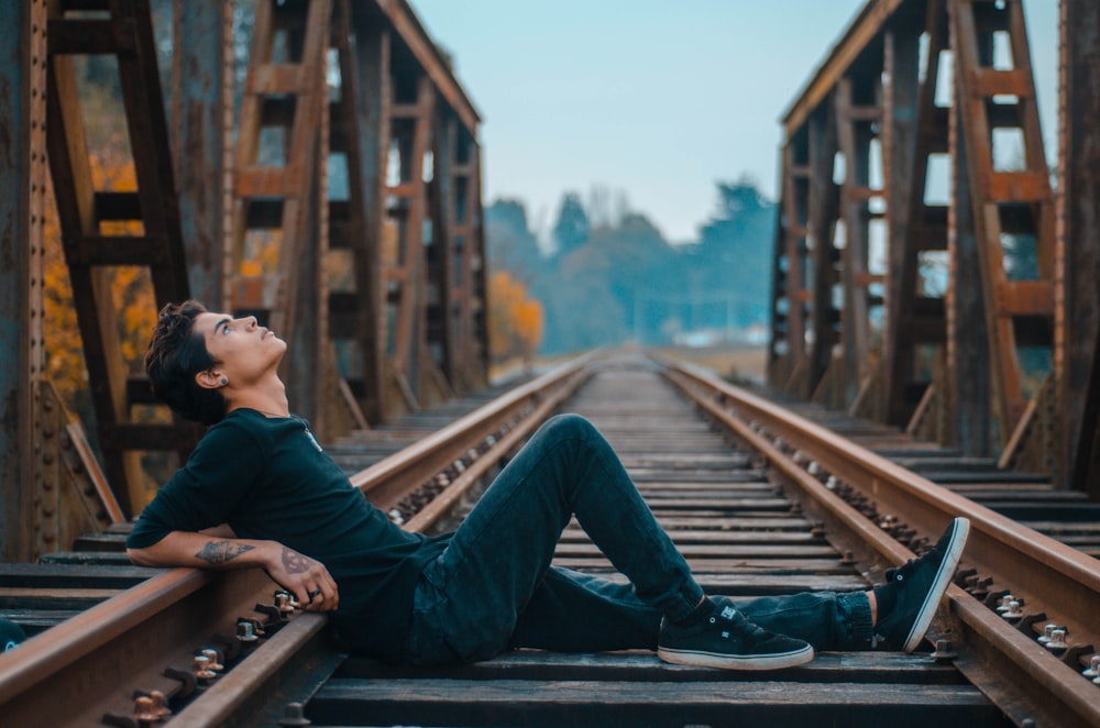 man sitting on railway looking up during daytime