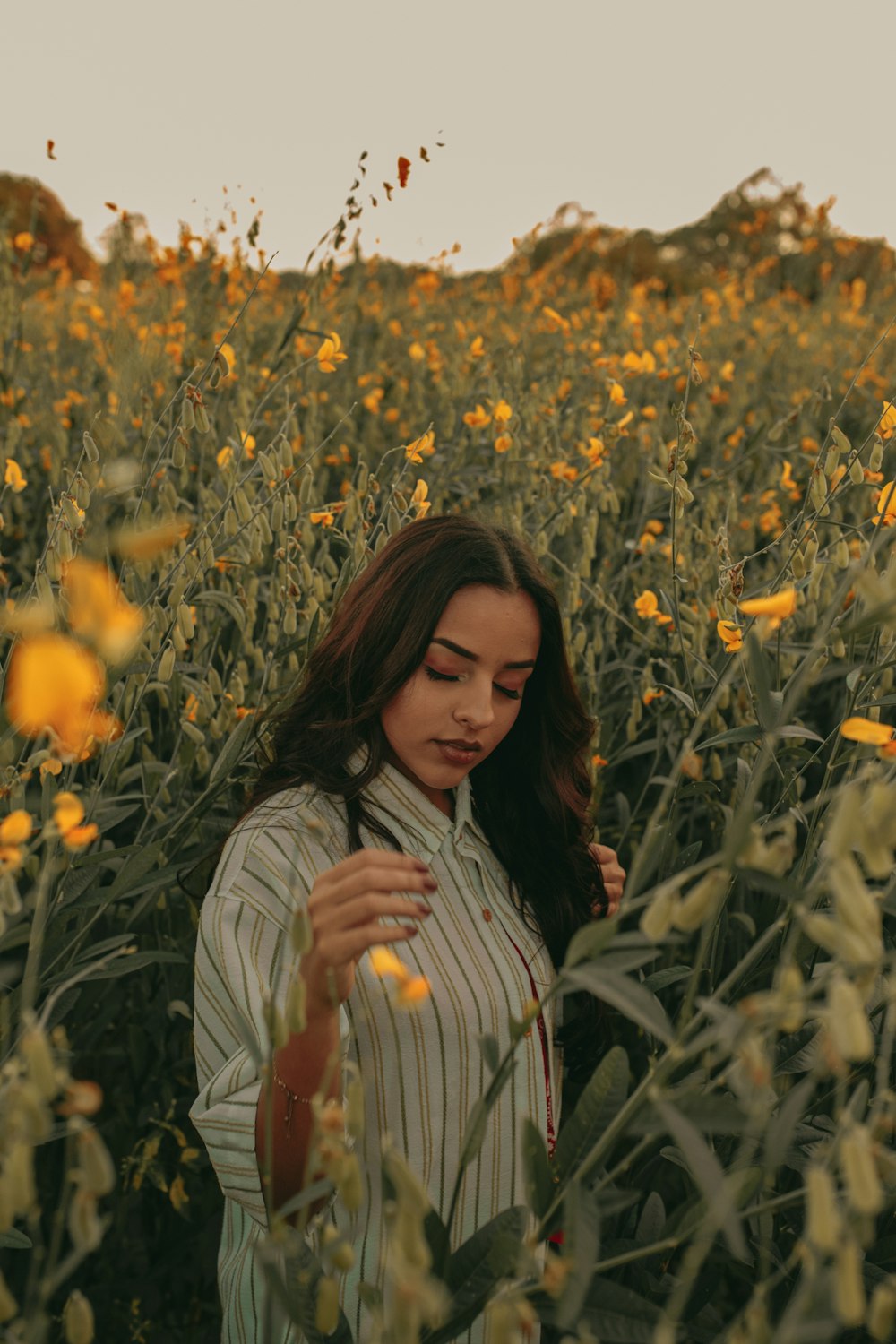 woman in pinstriped shirt standing between yellow flowers