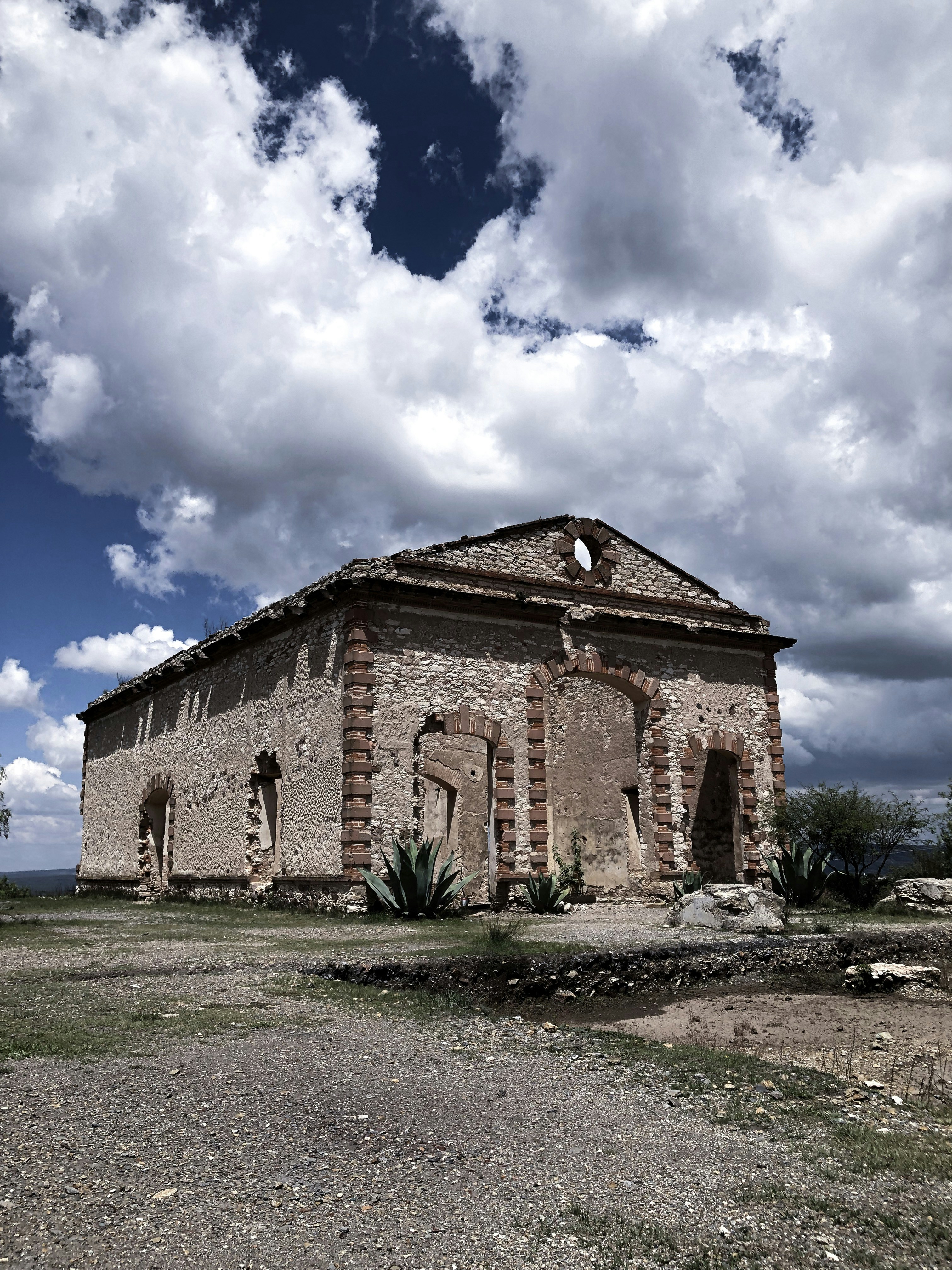 A photo of an abandoned stone building, with its entrances sealed, in a sunny day.