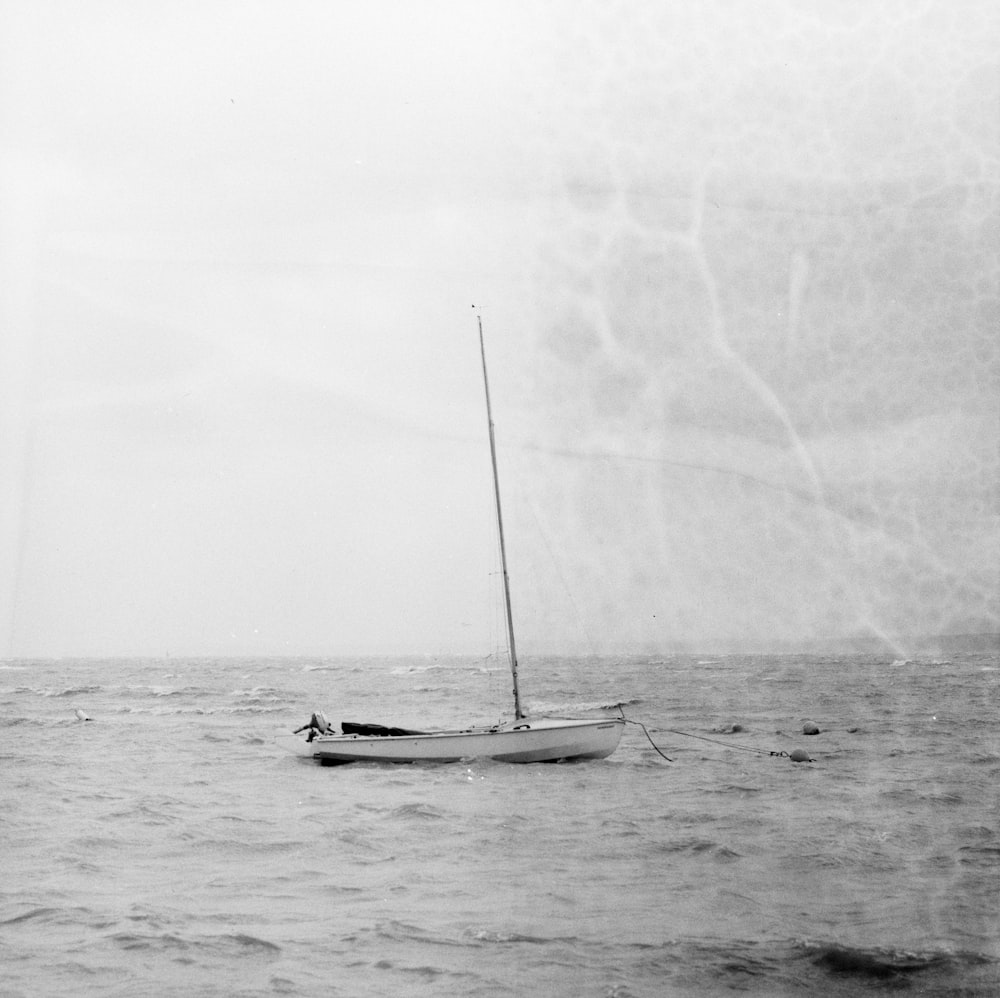 grayscale photo of sailboat anchored in beach