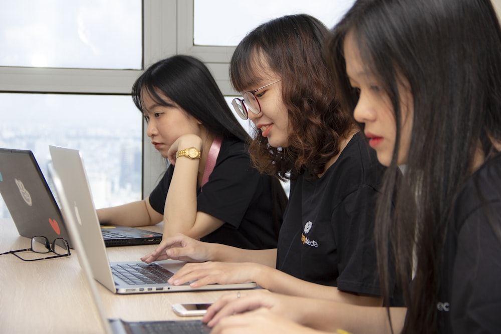 três mulheres sentadas ao lado de computadores portáteis fotografia close-up