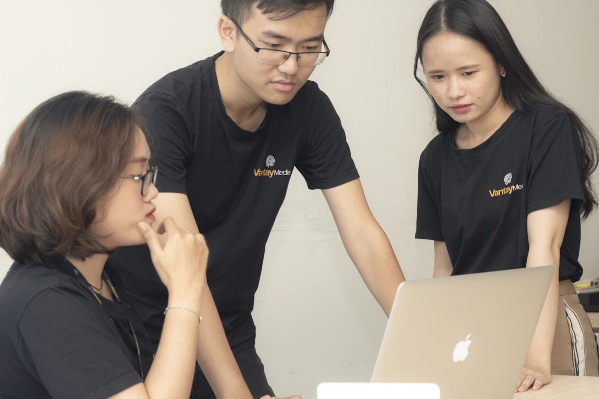 A senior colleague walking two teammates through something on-screen &mdash; the thinking passing from one person who shaped it to others who now carry it.