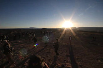 A group of families carrying belongings, walking through a rugged landscape at dusk.